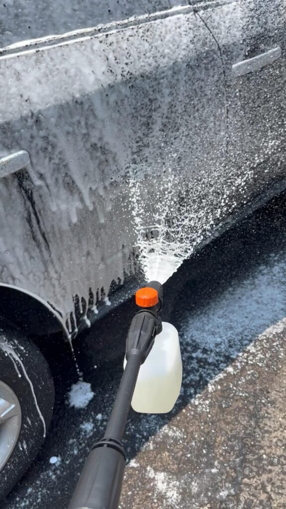 Lanza de espuma aplicando jabón al costado de un auto negro