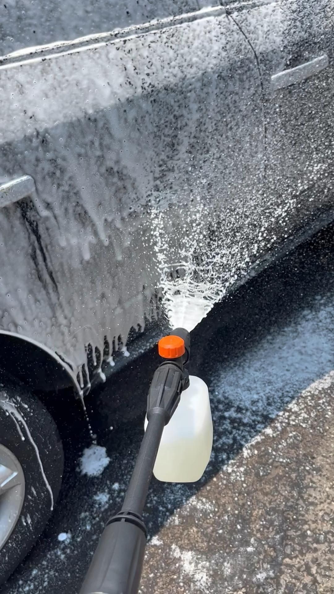 Lanza de espuma aplicando jabón al costado de un auto negro: lavado de coches a domicilio